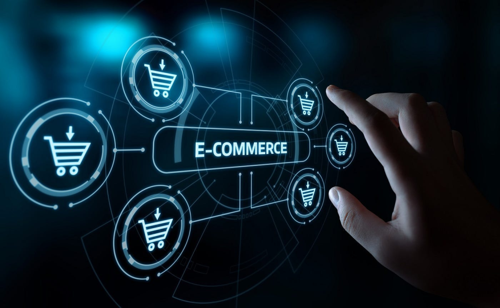 The image visually represents the concept of e-commerce using a futuristic digital interface. Here are the key elements:

Central Text:

The word "E-COMMERCE" is prominently displayed in the center, indicating the primary focus of the image.
Shopping Cart Icons:

Surrounding the central text are multiple shopping cart icons, symbolizing online shopping and transactions. These icons are connected by lines, suggesting a network or system.
Hand Interaction:

A hand is reaching out to interact with the interface, symbolizing user engagement with e-commerce platforms. This emphasizes the interactive nature of digital shopping.
Futuristic Design:

The overall design is sleek and modern, with glowing blue elements and a dark background, giving it a high-tech and futuristic feel.
Digital Interface Elements:

The image includes various circular and interconnected elements, representing a sophisticated and integrated digital system.
This image effectively conveys the idea of advanced e-commerce technologies and user interaction with online shopping platforms.