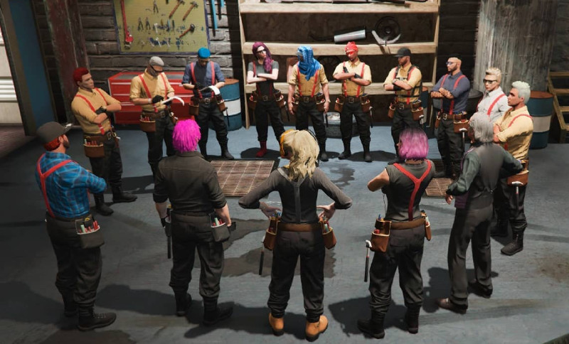 A group of people dressed in construction worker outfits standing in a circle, possibly having a discussion or meeting, in a workshop environment with tools and equipment visible in the background.