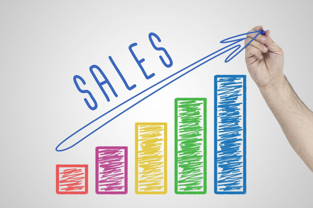 Hand drawing an upward arrow over a colorful bar chart labeled 'SALES,' symbolizing growth and increase in sales performance.