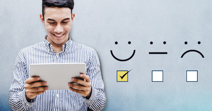 A man in a striped shirt is smiling while looking at a tablet he is holding. Next to him on the right side of the image, there are three feedback icons: a happy face, a neutral face, and a sad face. The happy face is checked with a yellow box, indicating positive feedback.