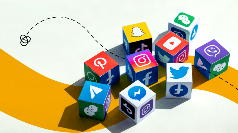 Colorful cubes with social media icons are scattered on a light surface. The cubes display logos of popular platforms such as Instagram, Twitter, Facebook, YouTube, Snapchat, and TikTok. A dashed line loops from the left side of the image toward the cubes, suggesting movement and connectivity. The background features a curved yellow stripe, adding a dynamic visual element to the composition.